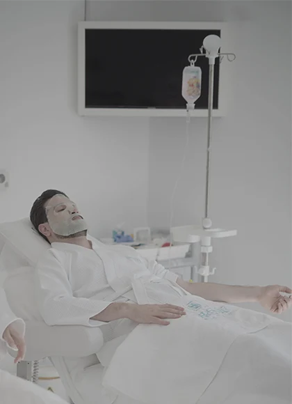 Hydration & Energy IV Therapy in Dubai 1 A man relaxing on a treatment chair receiving Hydration and Energy IV therapy at a modern wellness clinic in Dubai, wearing a white robe and facial mask in a calm, minimal setting.